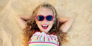 Top view of pretty little blonde girl in sunglasses lying on san Top view of pretty little blonde girl in sunglasses lying on san