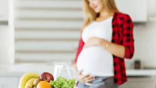 Young happy blurred pregnant woman on kitchen in red shirt, hold hand on belly,on front table bowl with mix fruits, healthy pregnancy concept Young happy blurred pregnant woman on kitchen in red shirt, hold hand on belly,on front table bowl with mix fruits, healthy pregnancy concept