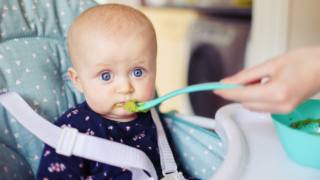 neonato mangia la prima pappa nel seggiolone