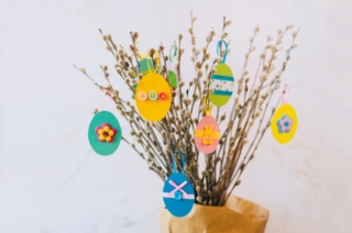 Easter eggs cutted from color paper decorated with ribbon and buttons on willow branches. Idea for DIY decoration with children. Selective focus on yellow paper egg. Easter eggs cutted from color paper decorated with ribbon and buttons on willow branches. Idea for DIY decoration with children. Selective focus on yellow paper egg.