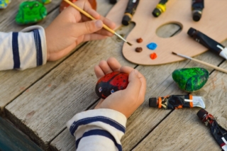A detailed picture of a child's hands drawing a ladybug on a stone with acrylic paints. Home hobbies are authentic. Artwork on stones. A detailed picture of a child's hands drawing a ladybug on a stone with acrylic paints. Home hobbies are authentic. Artwork on stones.
