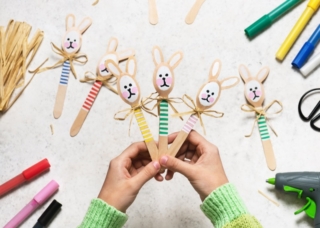Top view of three handmade colorful funny bunnies made from wooden spoons in child hands. Small gift or decor for Easter. Easy fun kids crafts concept. Top view of three handmade colorful funny bunnies made from wooden spoons in child hands. Small gift or decor for Easter. Easy fun kids crafts concept.