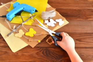 Child holds the scissors and cut out the felt flower. Scissors, hot glue gun, sheets of felt, decorative pendant with felt butterflies and flowers Child holds the scissors and cut out the felt flower. Scissors, hot glue gun, sheets of felt, decorative pendant with felt butterflies and flowers