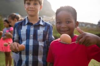 Portrait of boys playing egg and spoon race while standing in yard during party