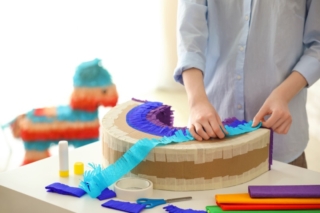 Woman making Mexican pinata in shape of rainbow at table
